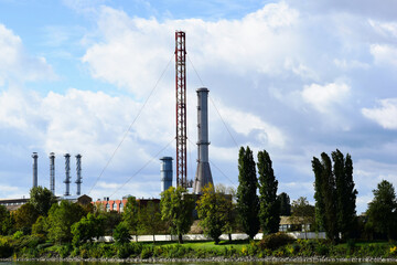 large industrial steel smoke stacks. blue sky. factory or plant. manufacturing, industry and energy production concept. tall steel truss communication tower with wire cable ties. lush green trees.