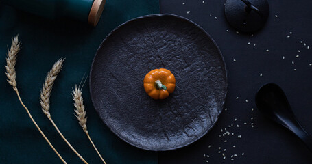 Little pumpkin on black plate with ears of wheat
