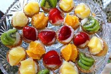 Colored mini tarts with strawberry, kiwi, orange and ananas on a table.