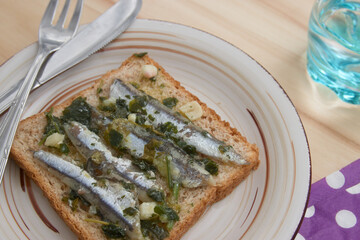 Flat lay of some anchovies seasoned with oil, vinegar, garlic and parsley on a plate