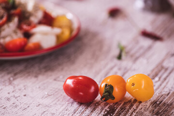 Three Cherry tomatos and caprese salad in the background on a kitchen table
