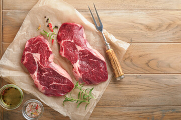 Raw beef steak. Marbled raw fresh Ribeye steak with rosemary, salt and pepper on cutting board on light old wooden background. Raw beef steak and spices for cooking. Mock up.