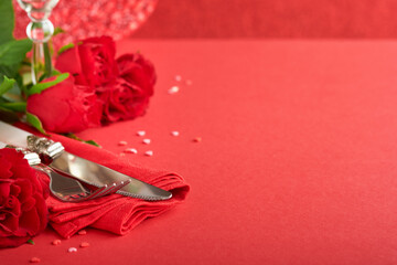 Romantic dinner concept. Romantic table setting, silverware, wine glasses, gift box, roses and symbol of love red heart on red background. Valentines Wedding Birthday Womens and Mothers Day.