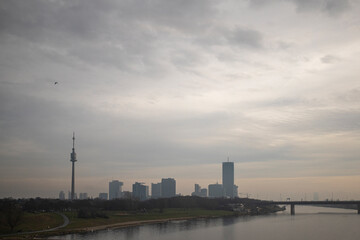 Obraz premium Photograph of the TV tower and Danube river in Donaustadt district, Vienna, Austria and a raven flying during a cloudy day.