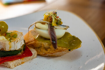 Board with typical snack of Basque Country, pinchos or pinxtos skewers with small pieces of bread, sea food, eggs, cheese served in bar in San-Sebastian or Bilbao, Spain
