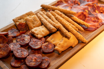 Wooden plate with sliced Spanish tapas, choriso sausage, lomo iberico en bread sticks