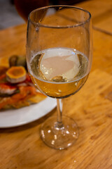 Board with typical snacks of Basque Country, pinchos or pinxtos, skewers or small piece of bread with toppings, served with glass of txakoli wine in bar in San-Sebastian or Bilbao, Spain