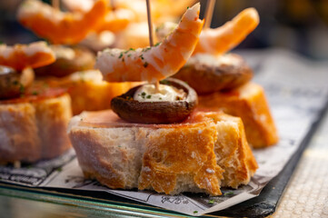 Typical snack of Basque Country, pinchos or pinxtos skewers with small pieces of bread, sea food, eggs, cheese, jamon served in bar in San-Sebastian or Bilbao, Spain