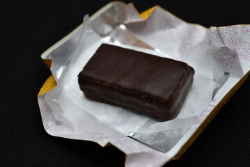 Chocolate candy in a package on a black background. Sweet candy. A chocolate bar in a paper package.