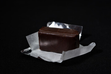 Chocolate candy in a package on a black background. Sweet candy. A chocolate bar in a paper package.