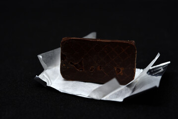 Chocolate candy in a package on a black background. Sweet candy. A chocolate bar in a paper package.