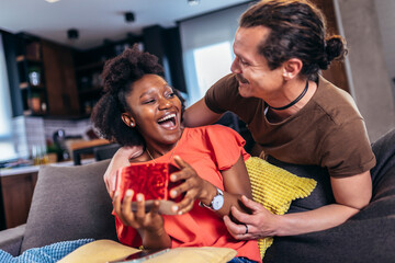 Surprised woman opening a present her boyfriend bought her for their anniversary.