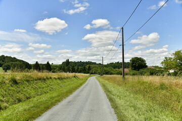 Fototapeta na wymiar Route secondaire de campagne entre les végétation et champs de blé près du Puy de Versac au Périgord Vert 