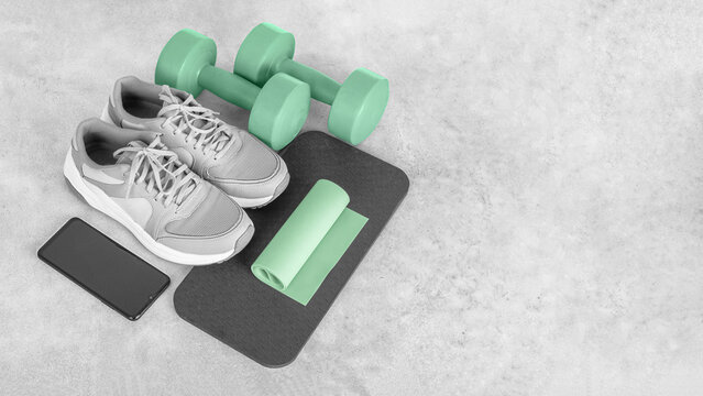 Fitness equipment on a gray concrete background. Sports shoes, smartphone, dumbbells, mat, exercise band, copy space. Fitness and activity. Smart fitness training. Home workout online.