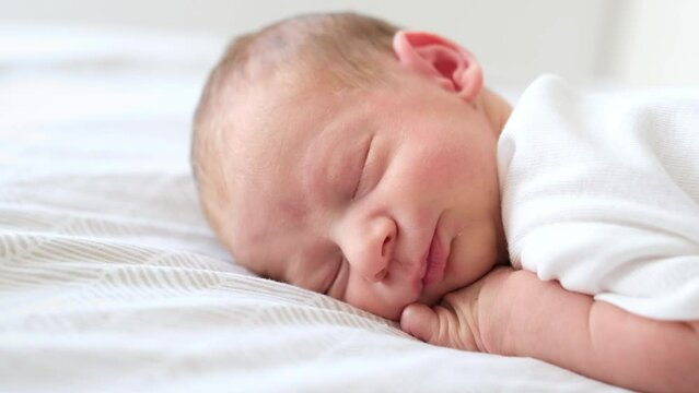 Cute adorable newborn baby boy lying on stomach on white bed at home sleeping,Purity,innosence concept.Close-up of face.