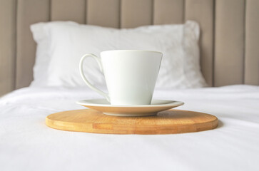 Fototapeta na wymiar cup of freshly brewed coffee stands on wooden tray on clean white bed. mate cups with morning coffee
