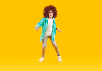Happy smiling preteen boy in curly red wig dancing. Excited boy wearing glasses, shirt, jeans and...