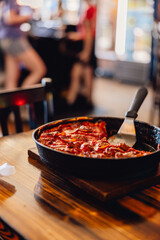 Chicago style pepperoni deep dish pizza on wooden table with serving tool in restaurant