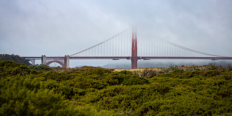 Fototapeta premium panorama of the golden gate bridge in san francisco during foggy weather; the famous red bridge emerging from behind the clouds, gloomy photo of the golden gate bridge