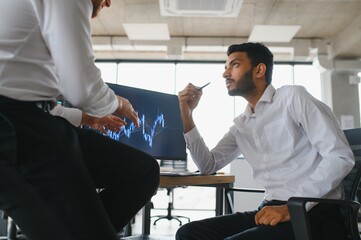 Two men traders sitting at desk at office together monitoring stocks data candle charts on screen analyzing price flow smiling cheerful having profit teamwork concept