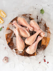 frozen raw chicken legs with vegetables on the ice on wooden board on the.gray rock background