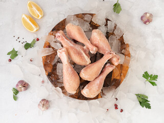 frozen raw chicken legs with vegetables on the ice on wooden board on the.gray rock background