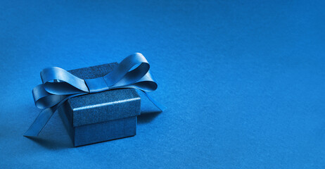 small Luxury gift box with a blue bow on dark blue. High angle view monochrome . Fathers day or Valentines day gift for him. Corporate gift concept or birthday party. Festive sale copy space