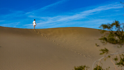 beautiful girl in short lace dress walking on the top of large sand dune in mesquite flat sand dunes, death valley, california, usa