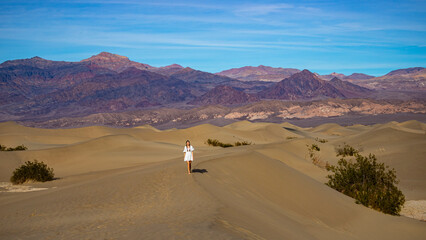 Fototapeta na wymiar Beautiful girl in white dress walk on large, vast and stunning Mesquite Flat Sand Dunes in Death Valley National Park, California State, USA. 