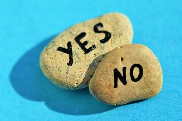 Two pebble stones with the text yes and no on a sunny blue table