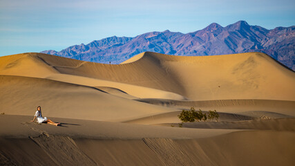 girl in white dress sits and relax on large sand dunes in mesquite flat sand dunes in death valley national park. Roadtrip in California, USA