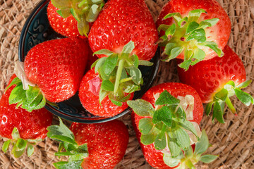 Background of strawberries with water drops in a bowl top view of a harvested berry on a straw lining, natural sunlight, strawberry spring season
