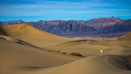 girl in white dress lost in the desert; walking on large sand dunes in mesquite flat sand dunes in death valley national park, california, usa