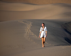 beautiful girl in lace dress lost in the middle of sandy desert; walking through mesquite flat sand dunes at sunset
