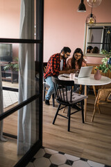 Young millennial indian husband and wife doing domestic paperwork, accounting job and reviewing paper bills, receipts at laptop computer, using online calculator and paying mortgage rent fees on
