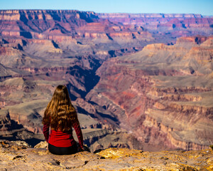 long haired hiker girl sitting on the edge of grand canyon; hiking in the grand canyon national...