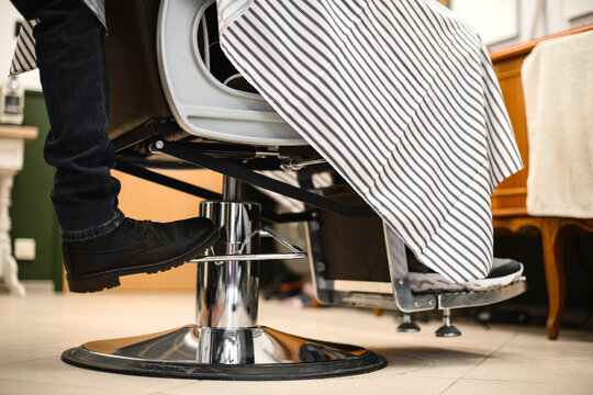 close-up view on male leg at adjusting lever of barbershop armchair.