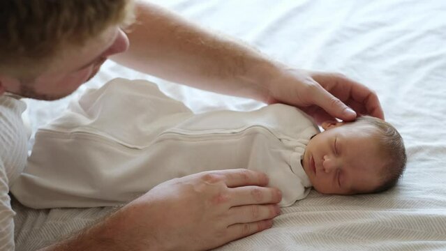 Few days old caucasian newborn baby sleeping on bed. Happy Fathers day concept.Man caressing baby, high angle view.Love and child care concept