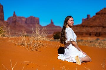 portrait of a girl in a lace dress sitting on the sand in monument valley with massive rocks in the background; cowgirl in the American desert in the wild west