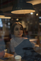 Beautiful cute young woman in a fashion black dress is sitting in a cafe near the window and drinking coffee.