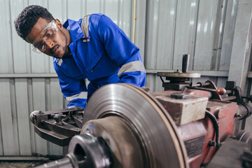 Obraz na płótnie Canvas African mechanic worker or metalworker using metal lathe machine operate polishing car disc brake at auto repair garage. Maintenance automotive and inspecting vehicle part concept