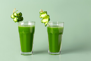 two glasses of celery juice with cucumber garnish on a green background