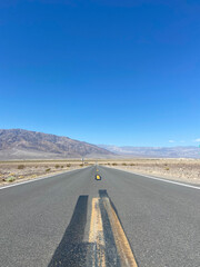 State Route 190 near the Devil's Cornfield area in Death Valley National Park, California, United States. Empty desert road in Death Valley with clear blue sky and rocky mountains.
