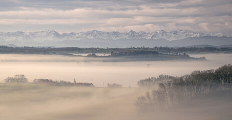 Obraz na płótnie Canvas Sunrise in the mist in the Gers department in France with the Pyrenees in the background