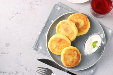 Homemade traditional Ukrainian dish syrniki with sour cream on grey plate on light background, Cottage cheese pancakes, Copy space
