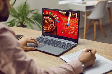 Man placing bets and writing notes while playing online casino at home on his laptop. Close up of...