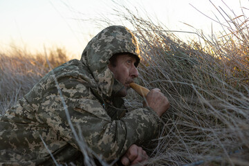 A mature hunter with a gun lures ducks by decoy while sitting in the reeds