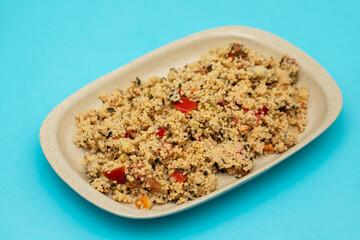 Couscous with vegetables in a dish on blue