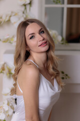 Naklejka premium beautiful long-legged fair-haired girl near a fireplace decorated with white orchids