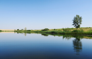 Reflection of the sky with clouds on the shore of a large lake on a sunny summer day.
